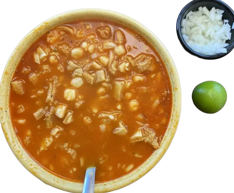 Bowl of red menudo with hominy, onion and lime
